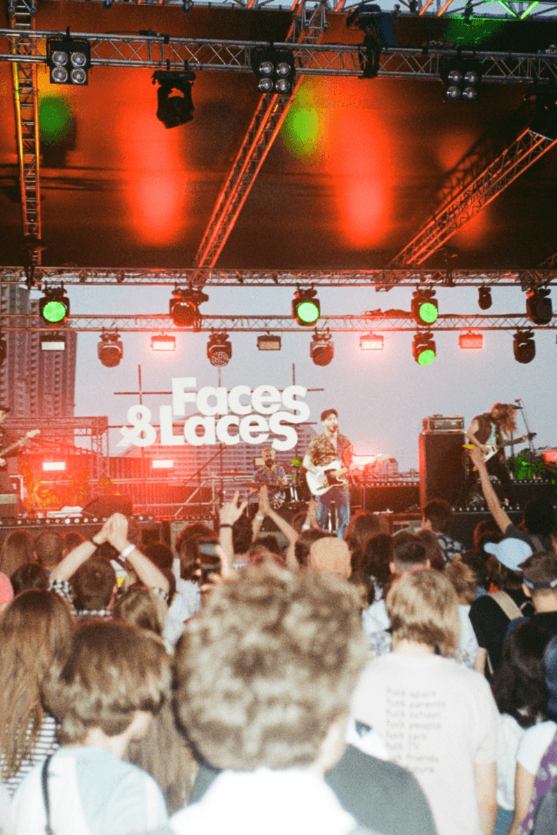 Outdoor festival crowd watching a band perform on a large stage with lighting rigs.