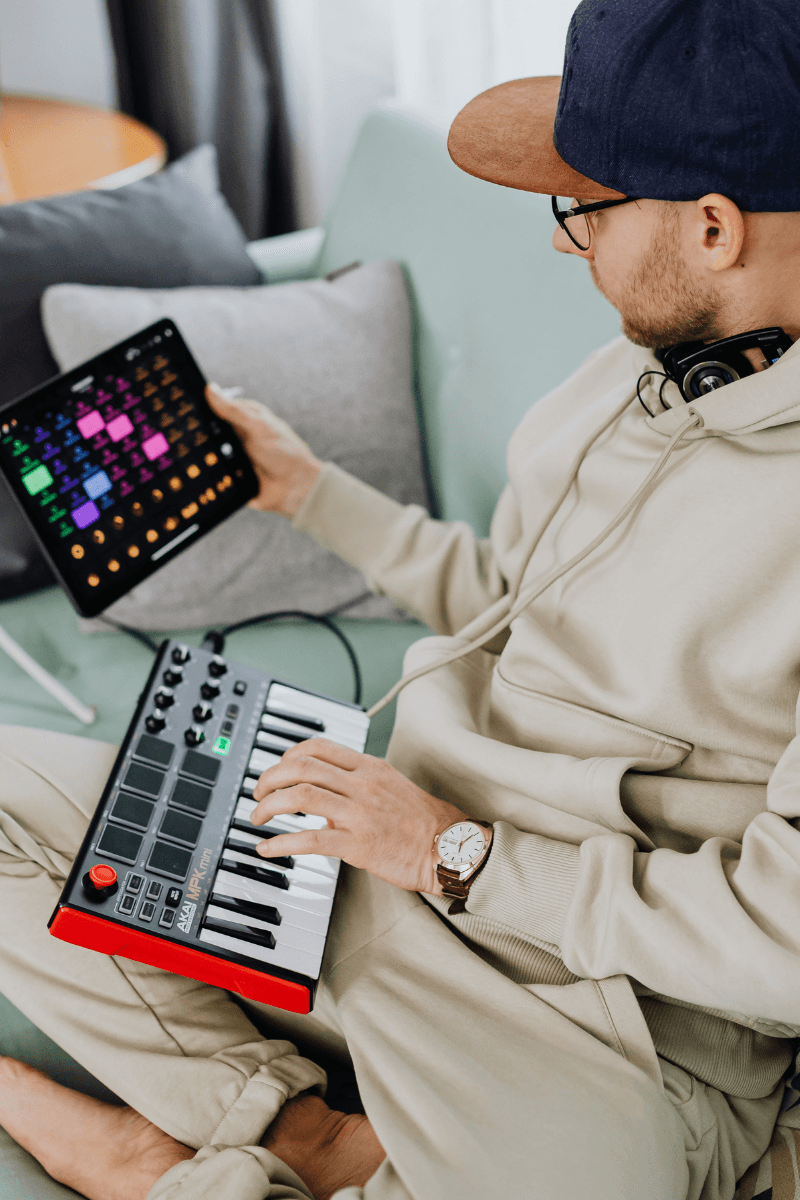 Music producer using a MIDI keyboard and tablet beat-making app in a home studio setup.